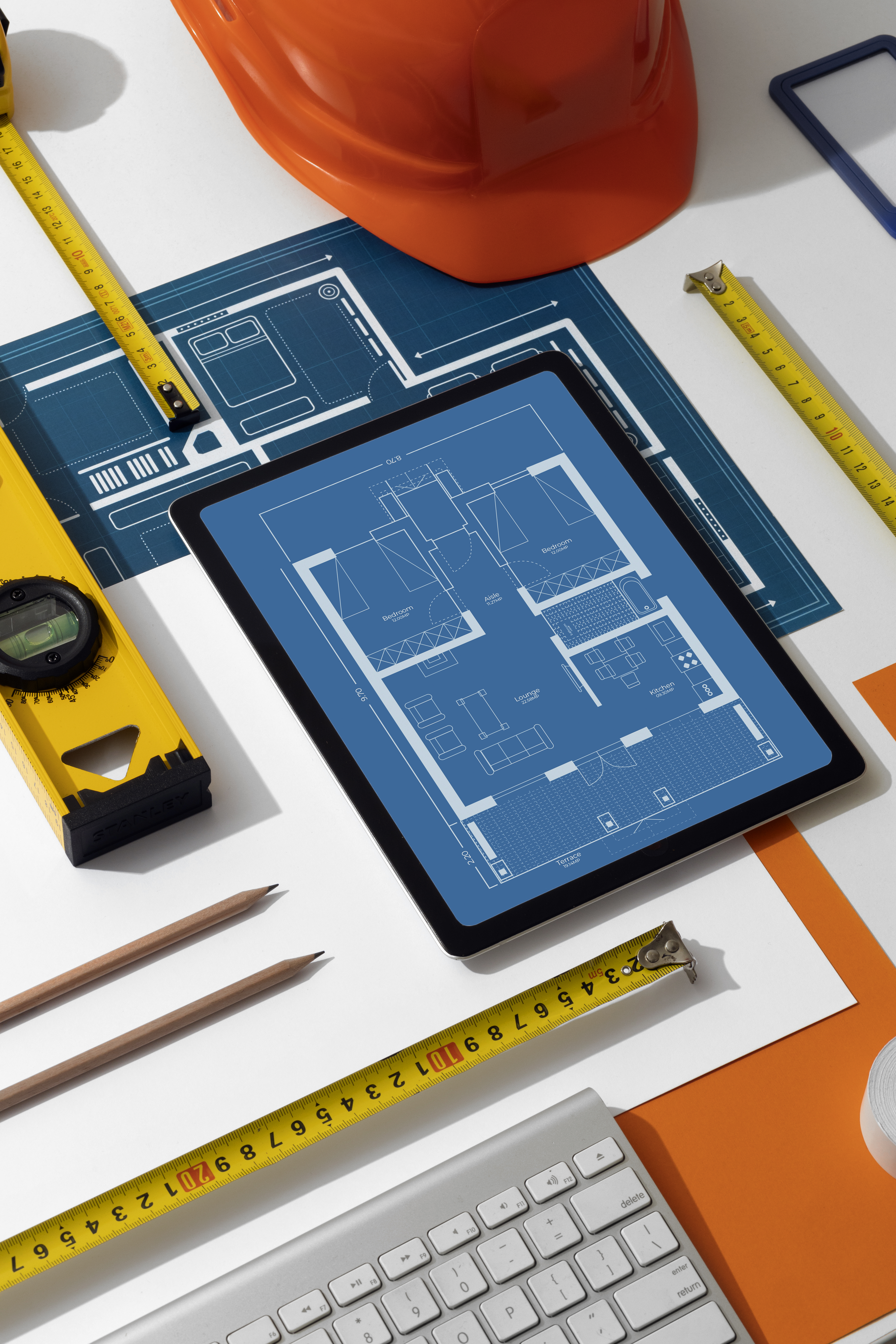 Architectural floor plans on a tablet beside a hard hat and measuring tools
